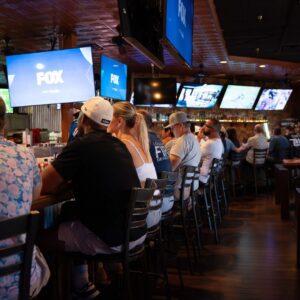 patrons sitting at bar, row of TVS
