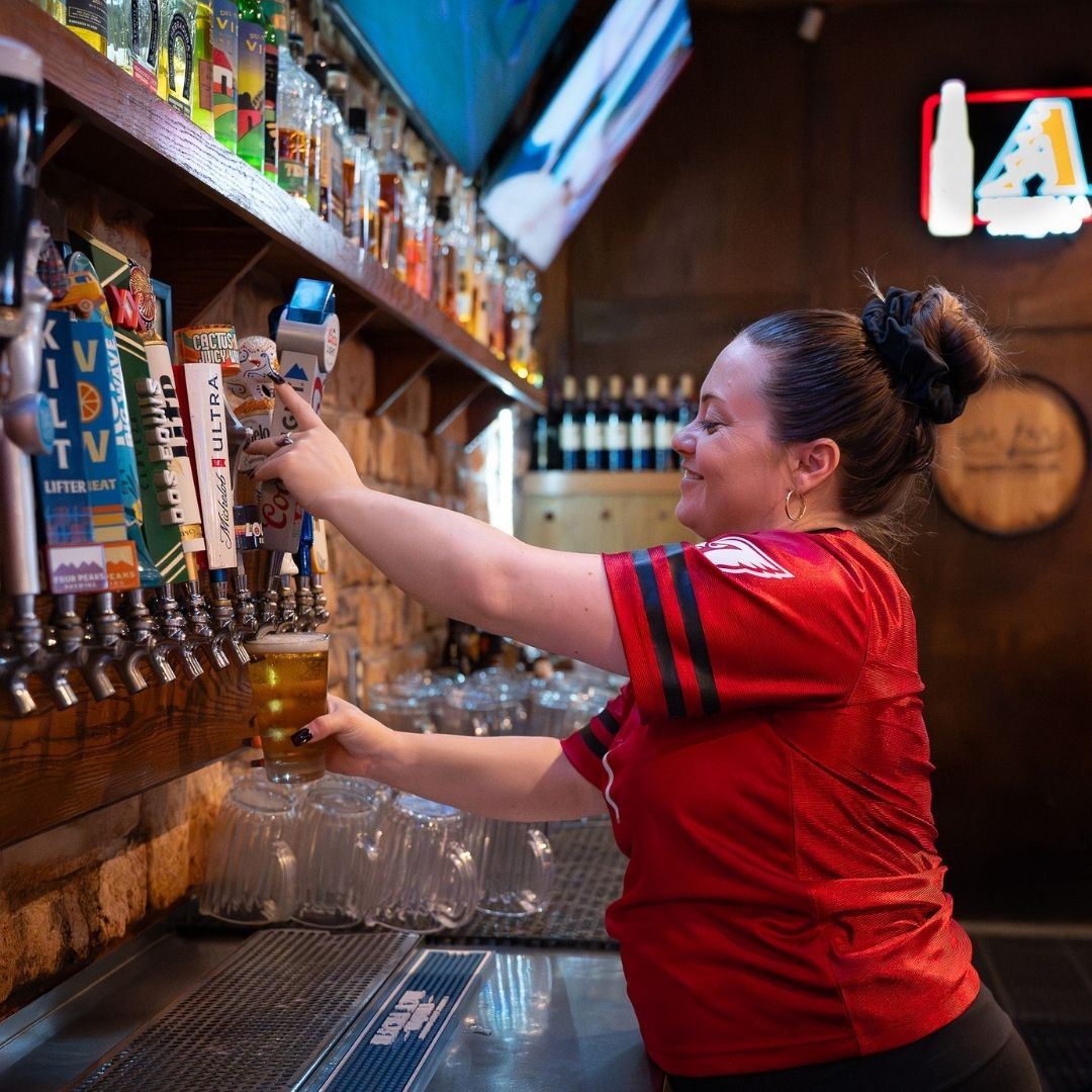 A bartender in a sports jersey pouring beer from a tap